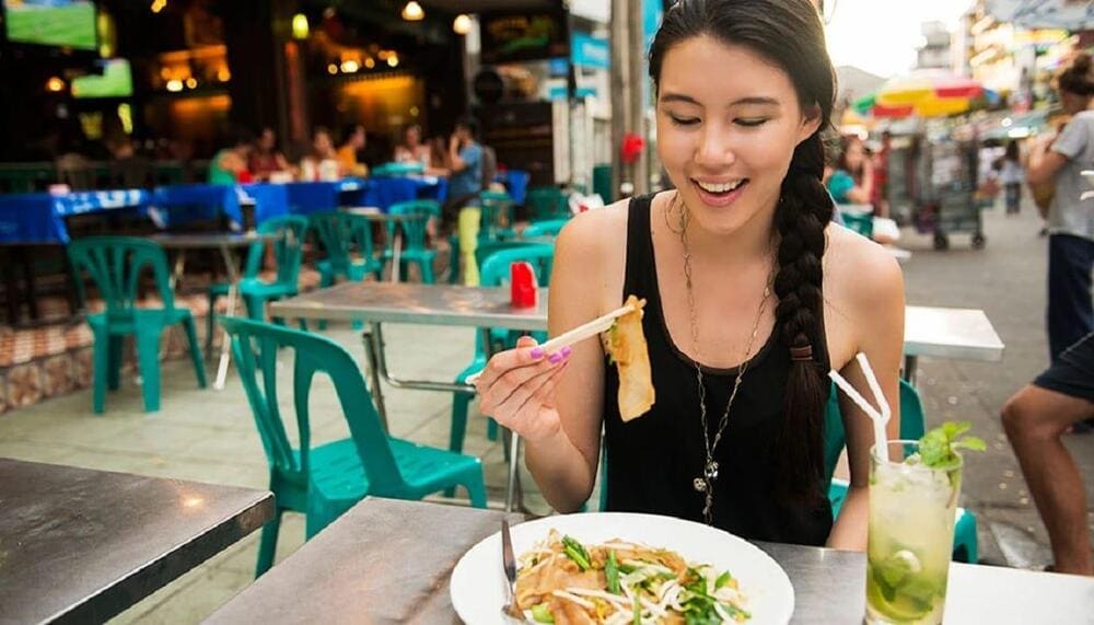 International tourists learning to eat Vietnamese food with chopsticks